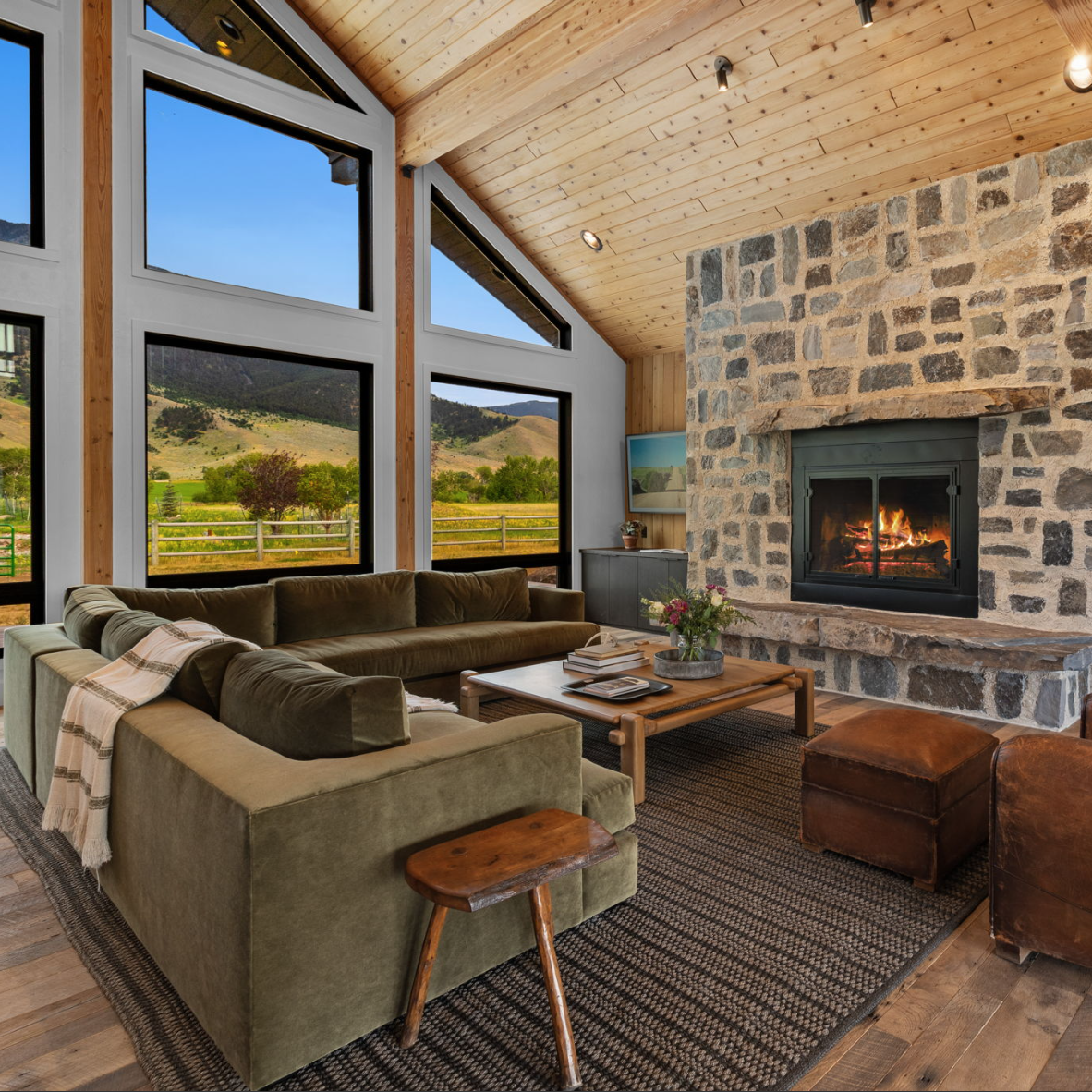cabin living area with a fireplace, couch, tall windows showing the Montana landscape
