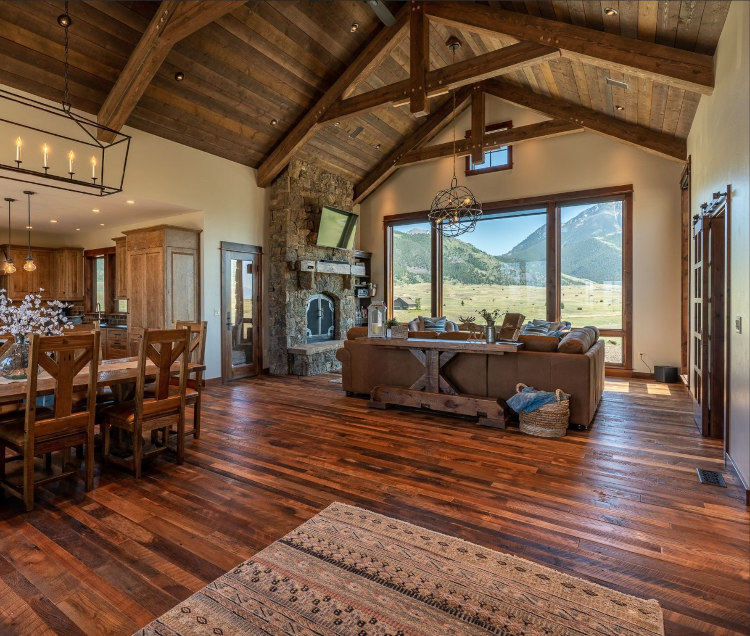 Open living and dining area in a Montana vacation rental, with a high wood-beamed ceiling, fireplace, dining table, kitchen, and mountain views