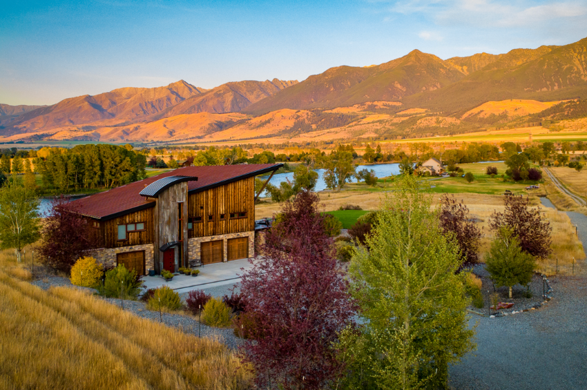 Our Yellowstone Beach Club property, one of many Yellowstone River vacation rentals offered by Key Montana. The property, a mix of wood and stone, is in the foreground, with the mountains in the background, bathed in the golden hour glow.